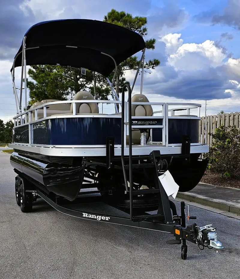 Slide: The Image of 2024 Ranger Reata 200F pontoon boat with canopy on trailer, parked outdoors. - 7