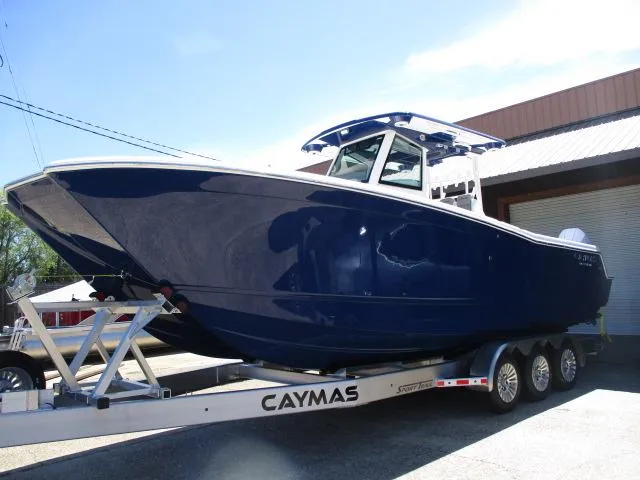Slide: The Image of 2024 Caymas 30CAT boat on trailer, sleek design, deep blue color, parked outdoors. - 2