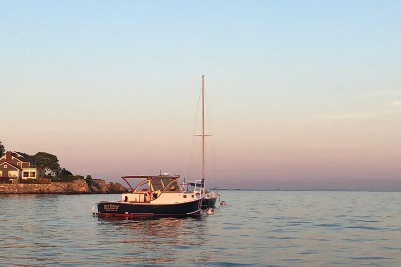 Slide: The Image of 1987 Harris Cuttyhunk Down East boat on calm water at sunset near coastal home. - 11