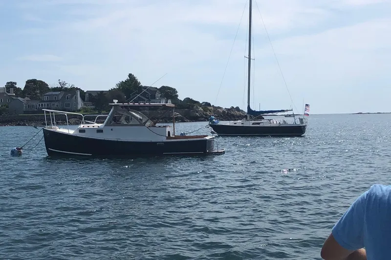 Slide: The Image of 1987 Harris Cuttyhunk Down East boat on calm water near a sailboat and shoreline. - 12