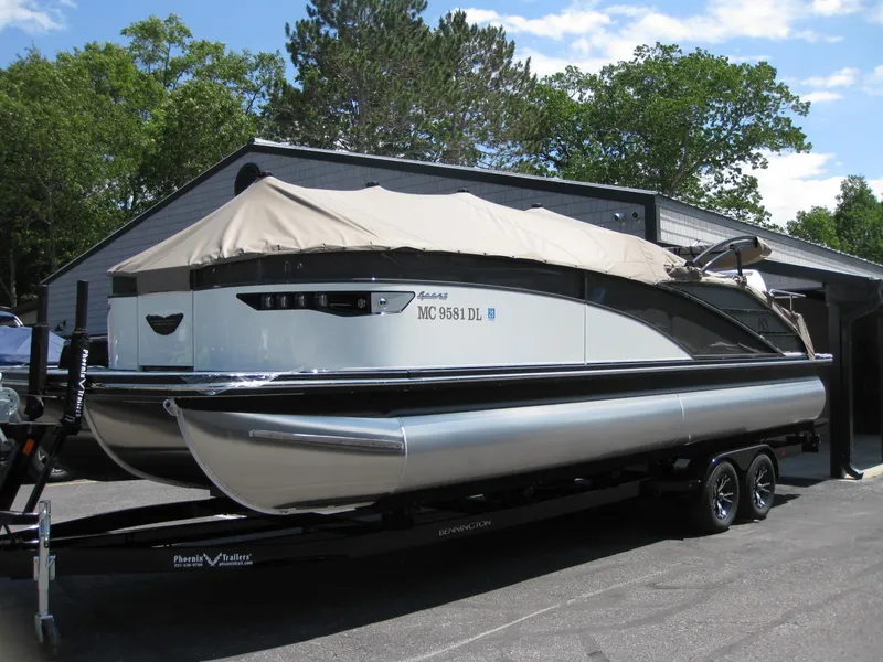 Slide: The Image of 2024 Bennington 25RX Swingback Windshield pontoon boat on trailer, covered and parked outdoors. - 1