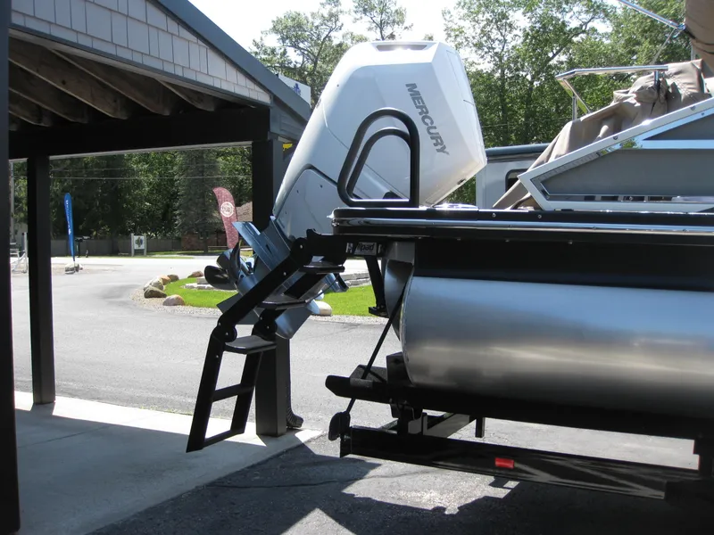 Slide: The Image of 2024 Bennington 25RX Swingback Windshield with Mercury outboard motor, parked under a shelter. - 17
