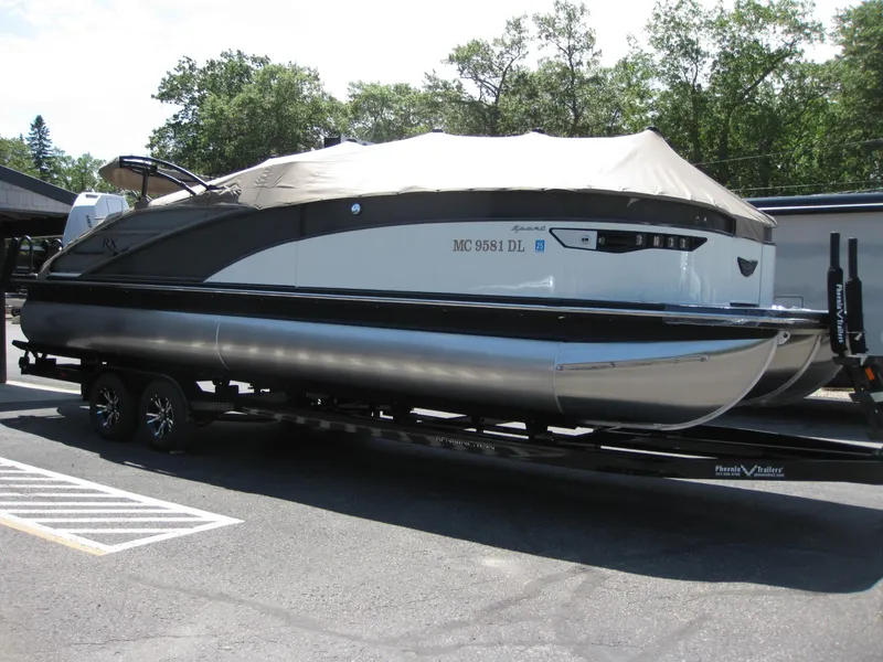 Slide: The Image of 2024 Bennington 25RX Swingback Windshield pontoon boat on trailer, parked outdoors. - 5