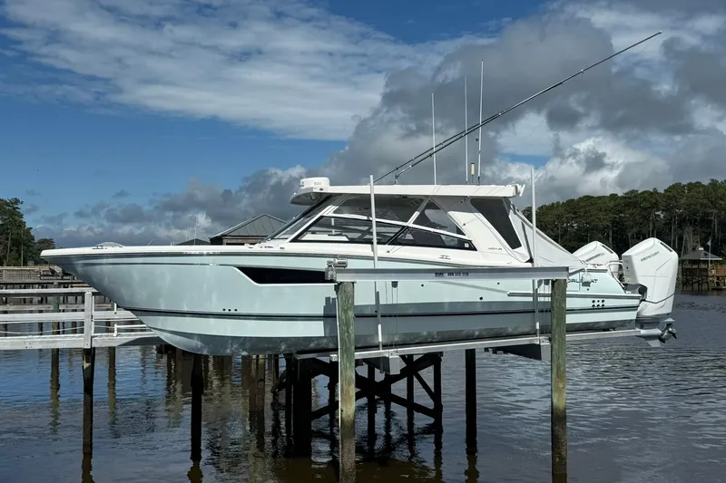 Slide: The Image of 2023 World Cat 400 DC-X boat on lift, dockside, under cloudy sky. - 2