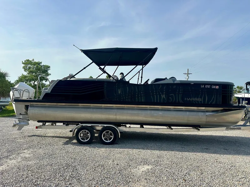 Slide: The Image of 2021 Harris Grand Mariner 250 pontoon boat on a trailer, parked on gravel. - 6