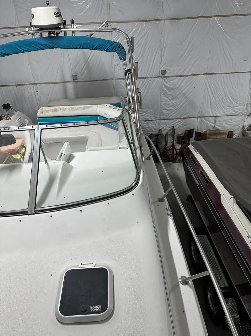 Slide: The Image of 1993 Rinker 280 Fiesta Vee boat in storage, featuring a blue canopy and white deck. - 14