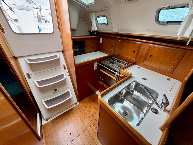 Slide: The Image of Interior of 2001 Beneteau Oceanis 331 sailboat, featuring a compact kitchen with wood cabinetry. - 10