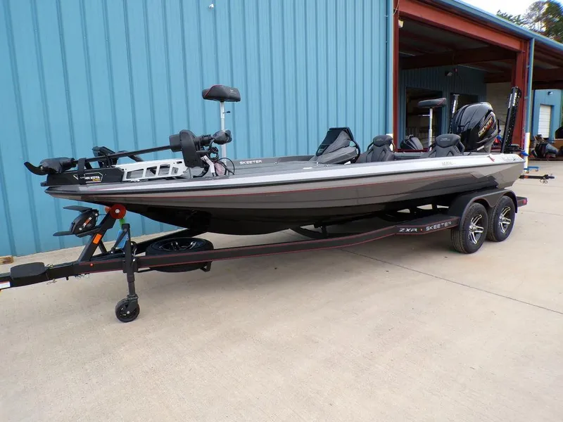 Slide: The Image of 2025 Skeeter ZXR21 bass boat on trailer, parked outside a blue building. - 5