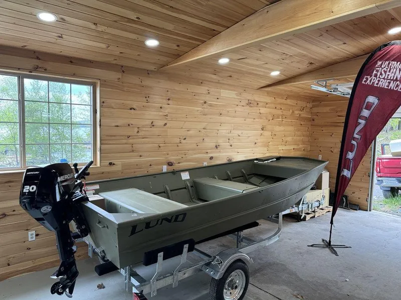 Slide: The Image of 2024 Lund 1448 Jon Tiller boat in wooden garage with Mercury outboard motor. - 2