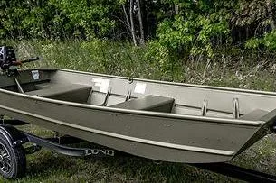 Slide: The Image of 2024 Lund 1448 Jon Tiller boat on trailer, parked near lush green trees. - 3