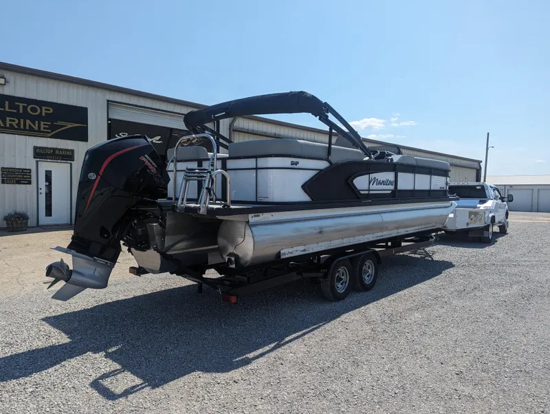 Slide: The Image of 2022 Manitou Encore 25 RF pontoon boat on trailer, parked outside a marine dealership. - 6