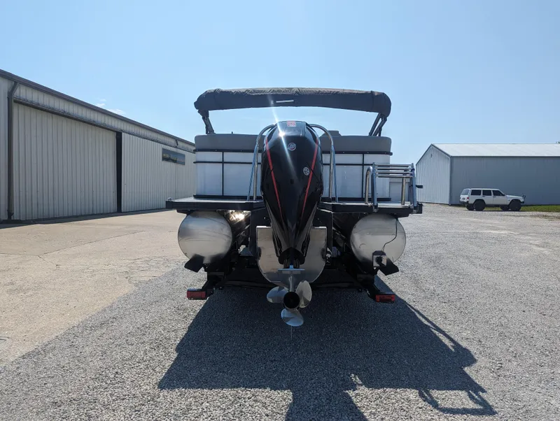 Slide: The Image of 2022 Manitou Encore 25 RF pontoon boat, rear view, parked on gravel near warehouses. - 7