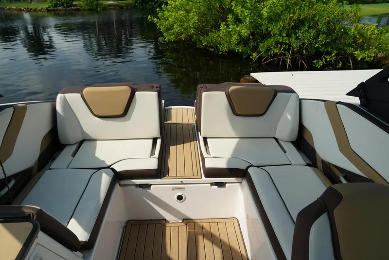 Slide: The Image of 2021 Yamaha Boats 252SE interior with cushioned seating and wood accents by the water. - 18