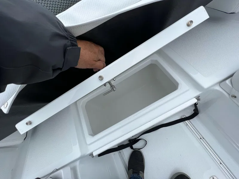 Slide: The Image of 2023 Wellcraft 262 Fisherman storage compartment with open lid and hand accessing interior. - 33