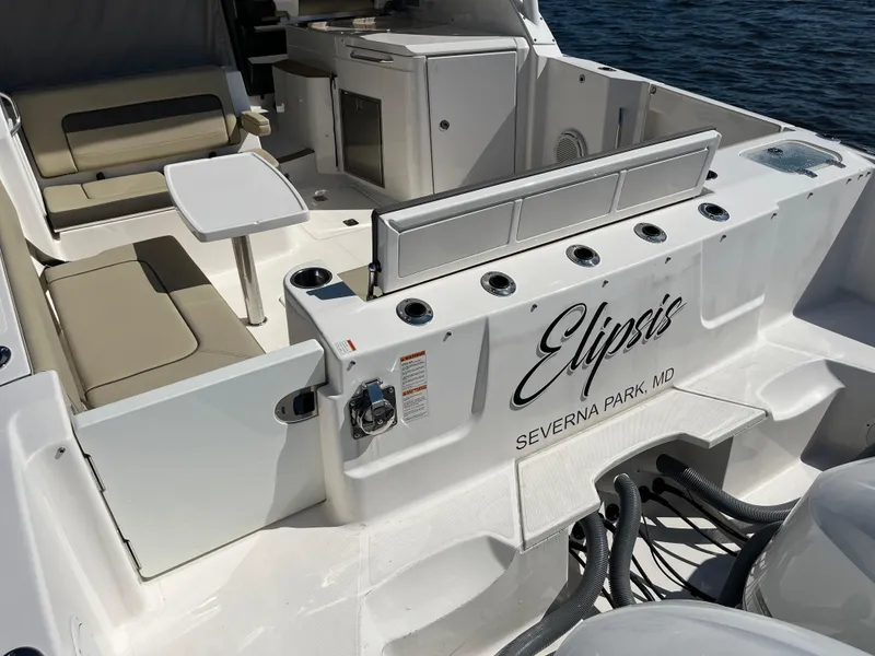 Slide: The Image of 2018 Pursuit DC 365 Dual Console boat interior with seating and table, docked on water. - 11