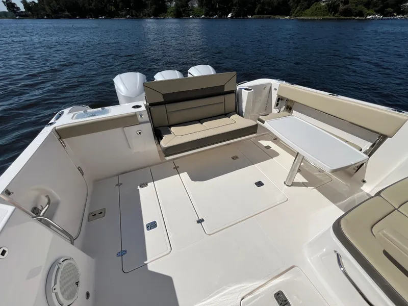 Slide: The Image of 2018 Pursuit DC 365 Dual Console boat interior with seating and table on a lake. - 12
