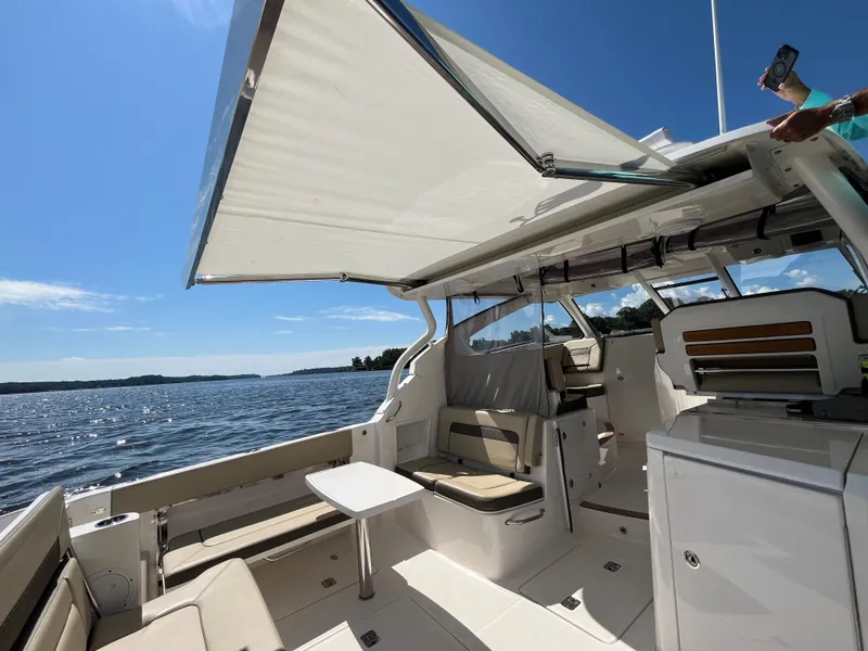 Slide: The Image of 2018 Pursuit DC 365 Dual Console boat with open canopy on a sunny day. - 18