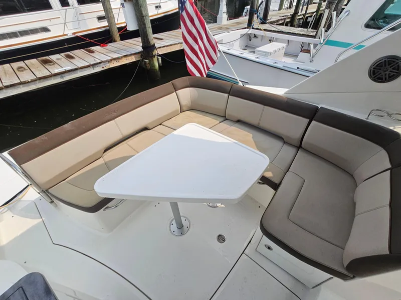 Slide: The Image of 2014 Sea Ray 350 Sundancer boat with cushioned seating and table, docked at marina. - 12