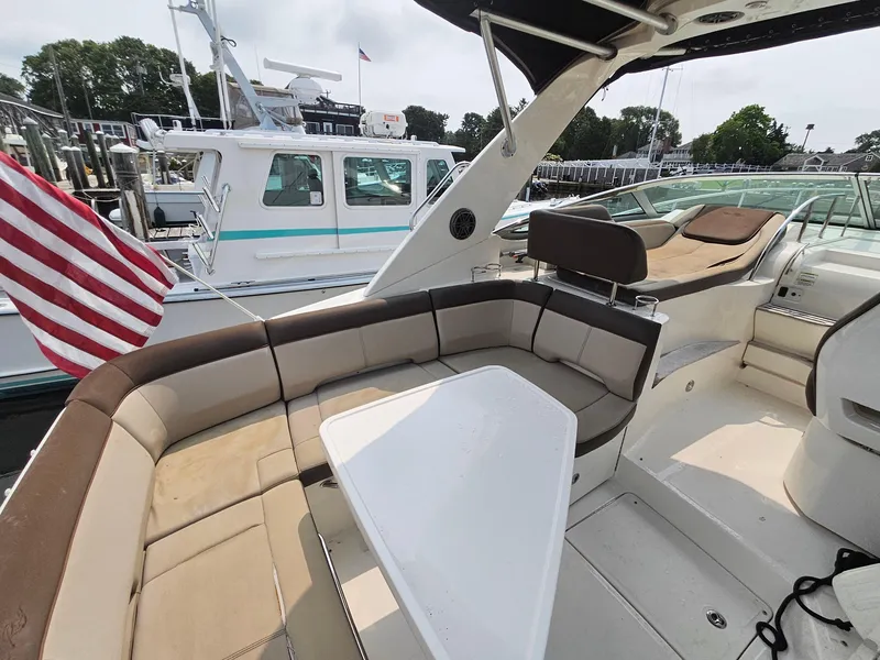 Slide: The Image of 2014 Sea Ray 350 Sundancer boat with spacious seating and table, docked near other vessels. - 13