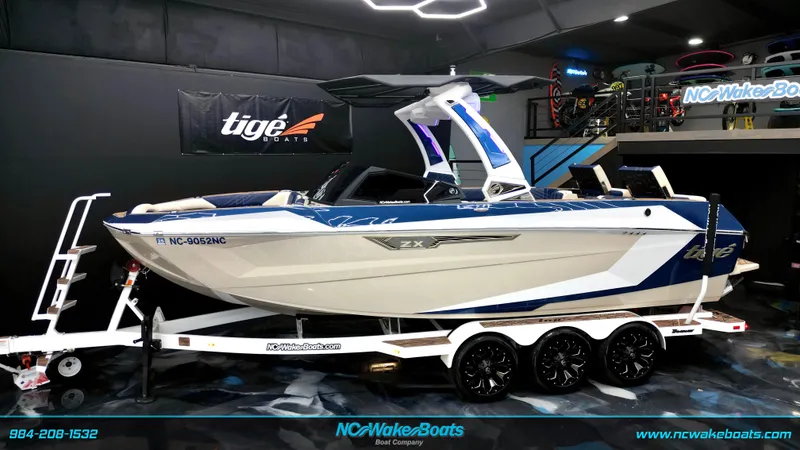 The Image of 2024 Tigé Ultré 23ZX boat on trailer in showroom, blue and white design. - 0