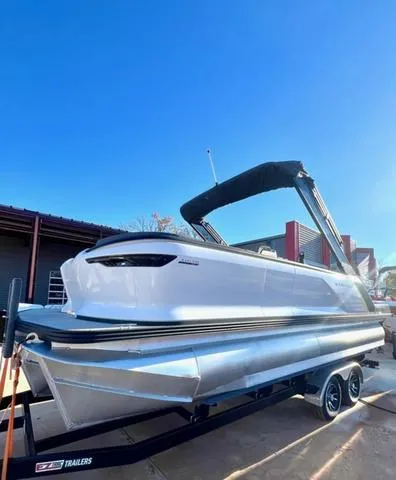 Slide: The Image of 2023 Manitou EXPLORE 22 pontoon boat with canopy, parked on a trailer under clear blue sky. - 3