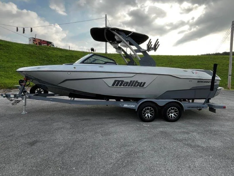 Slide: The Image of 2020 Malibu 25 LSV boat on trailer, parked outdoors under cloudy sky. - 3