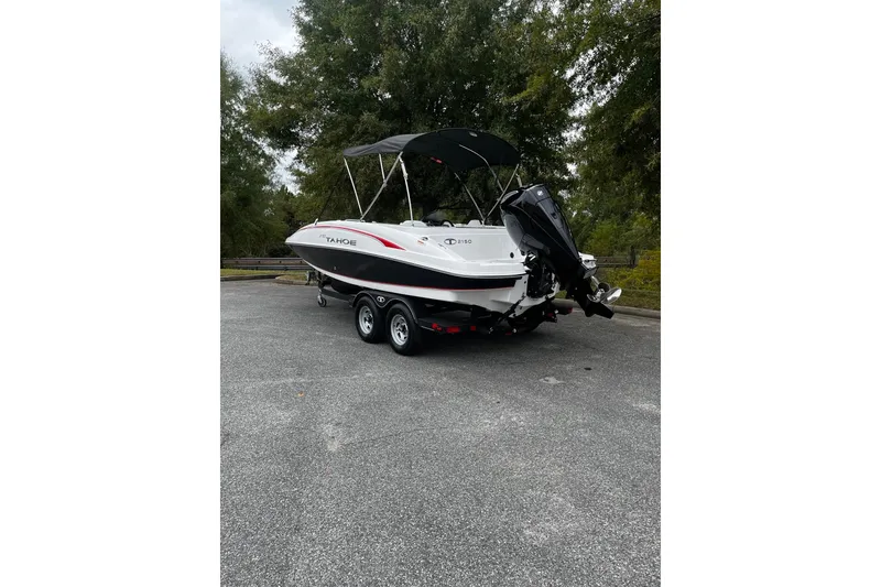 Slide: The Image of 2024 Tahoe 2150 boat on trailer, parked outdoors with trees in the background. - 2