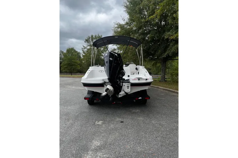 Slide: The Image of 2024 Tahoe 2150 boat with canopy, parked on a paved area, surrounded by trees. - 3