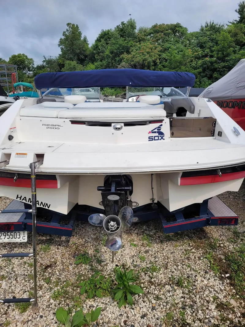 Slide: The Image of 2008 Regal ES2000 boat with blue canopy, parked on gravel, surrounded by greenery. - 14