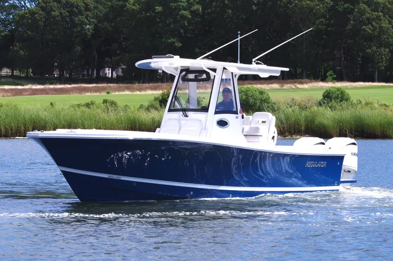 The Image of 2025 Regulator 28 boat cruising on a calm river with lush greenery. - 0