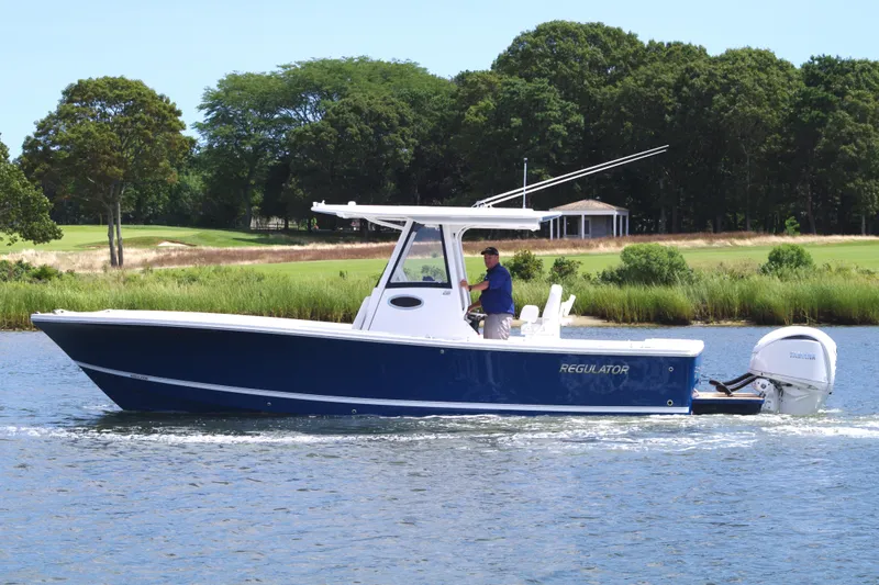 Slide: The Image of 2025 Regulator 28 boat cruising on a scenic lake with lush greenery. - 2