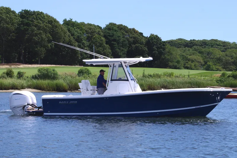 Slide: The Image of 2025 Regulator 28 boat cruising on a calm lake with lush green background. - 8