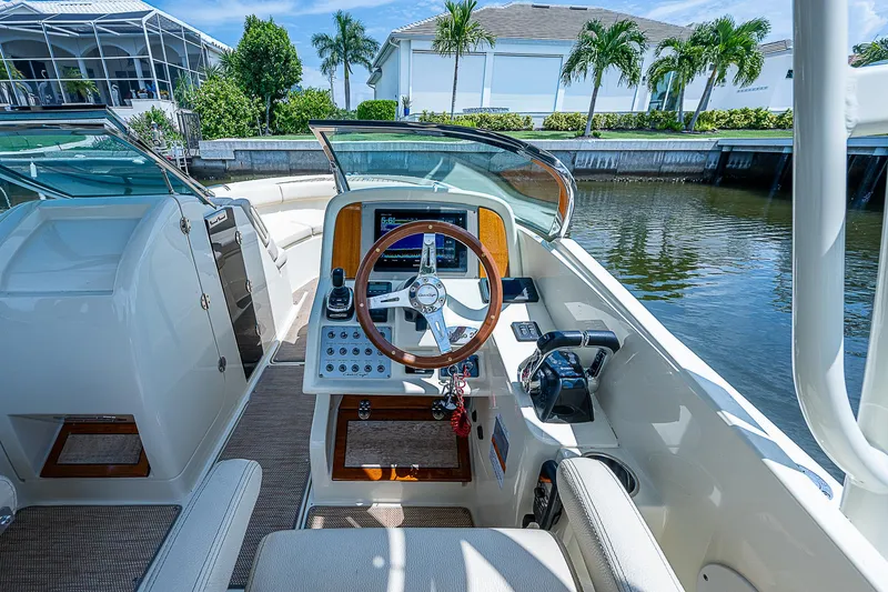 Slide: The Image of 2018 Chris-Craft Calypso 26 boat cockpit with steering wheel and controls, docked by water. - 11
