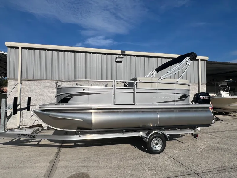 Slide: The Image of 2025 Starcraft LX 18 F pontoon boat on trailer, parked outdoors. - 2