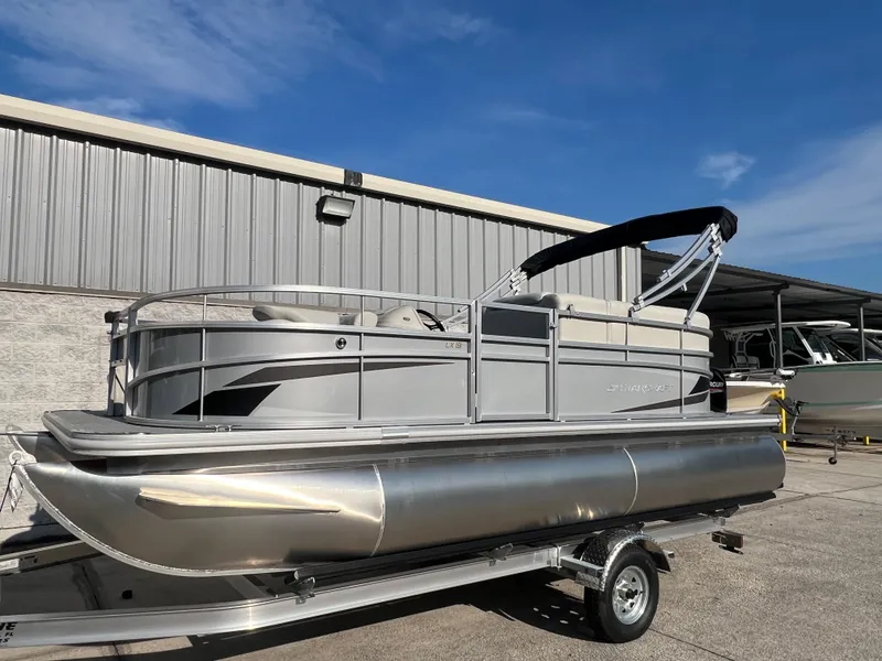 Slide: The Image of 2025 Starcraft LX 18 F pontoon boat on trailer, parked outdoors under blue sky. - 3