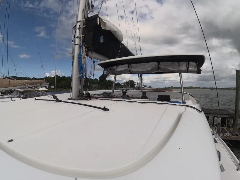 Slide: The Image of 2019 Lagoon 42 catamaran docked, featuring sleek deck and sail, under partly cloudy sky. - 42