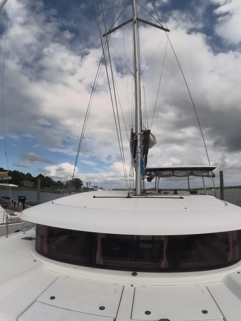 Slide: The Image of 2019 Lagoon 42 catamaran with sails, under a cloudy sky, docked by the shore. - 43