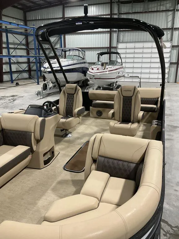 Slide: The Image of 2025 Harris Sunliner 230 Sport SLDH pontoon boat with luxurious seating in a spacious indoor showroom. - 3