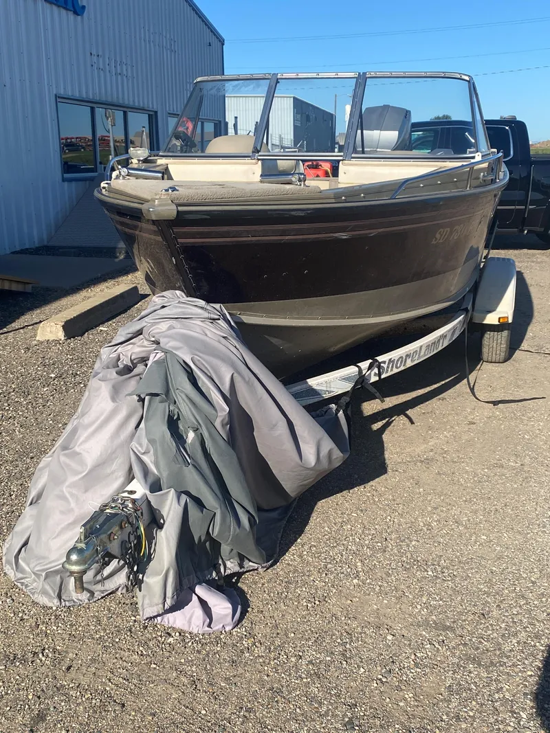 Slide: The Image of 1994 Lund 1850 Tyee boat on trailer, parked outdoors with cover partially removed. - 13