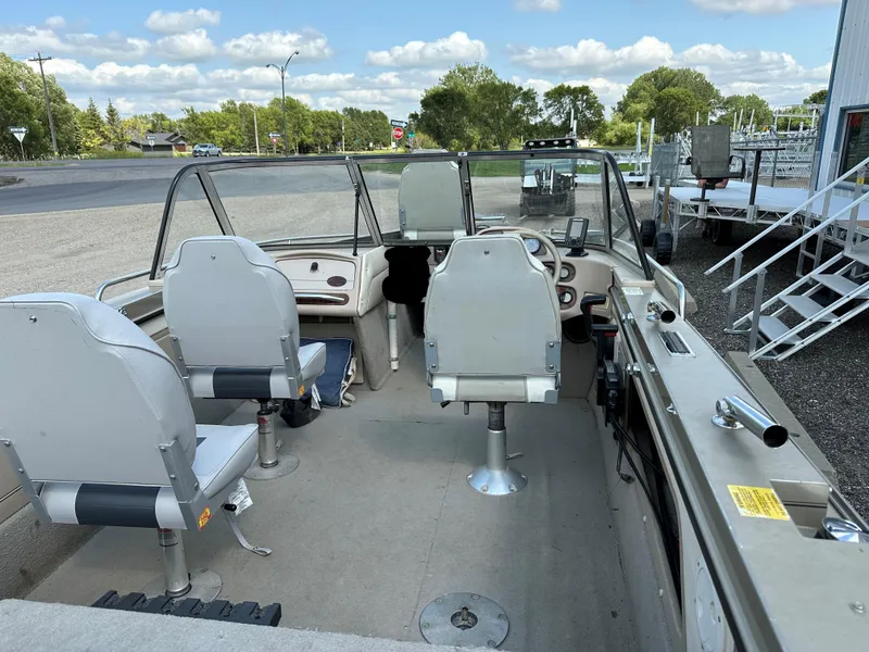 Slide: The Image of 1994 Lund 1850 Tyee boat interior with seating and steering wheel, parked outdoors. - 4
