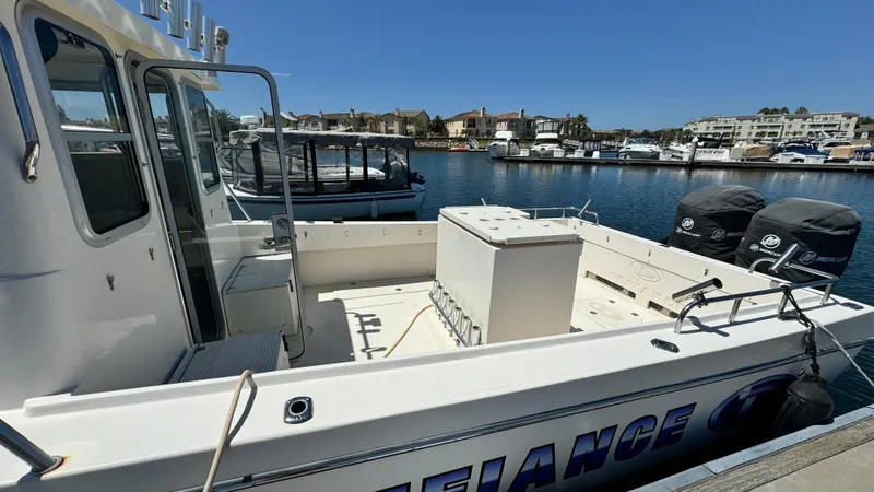 Slide: The Image of 2014 Defiance Guadalupe 290 EX boat docked in marina, featuring spacious deck and twin outboard motors. - 6