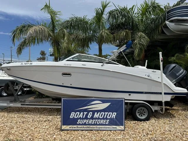 Slide: The Image of 2018 Four Winns HD240 OB boat on trailer at dealership, surrounded by palm trees. - 1