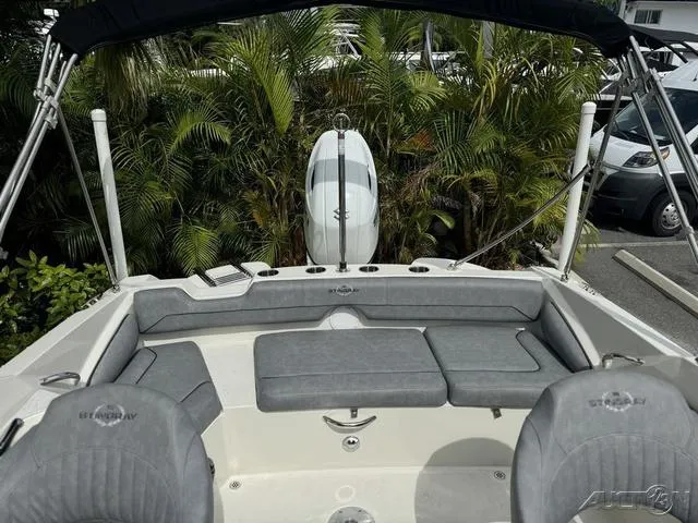 Slide: The Image of 2021 Stingray 201DS boat interior with gray seating and lush greenery background. - 23