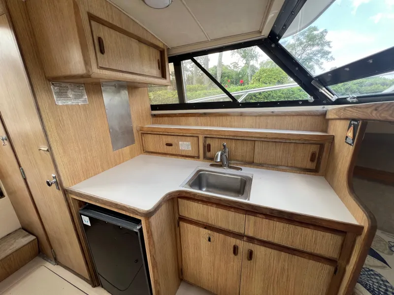 Slide: The Image of 1990 Bertram 28 Flybridge kitchen with wood cabinetry, sink, and compact fridge. - 31