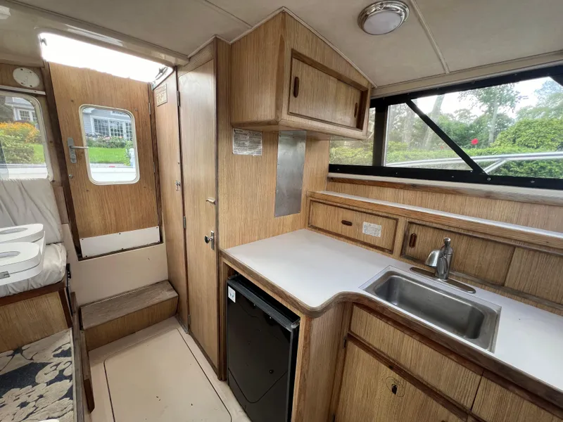 Slide: The Image of Interior of a 1990 Bertram 28 Flybridge boat, featuring a compact kitchen area. - 32