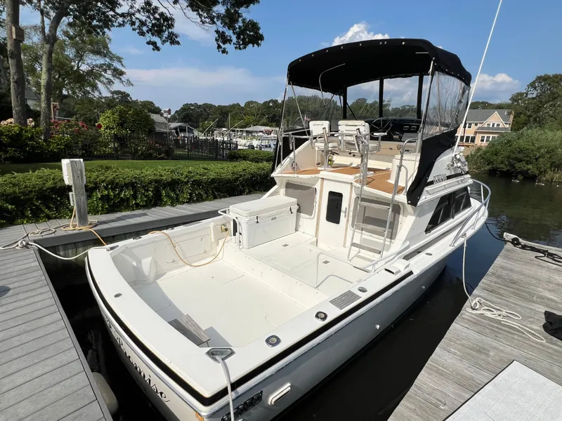 Slide: The Image of 1990 Bertram 28 Flybridge boat docked, featuring spacious deck and canopy. - 49