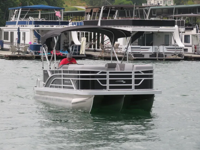 Slide: The Image of 2025 Bennington 20SVL-SPS pontoon boat cruising on a lake near a marina. - 6