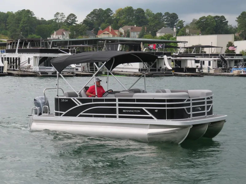 Slide: The Image of 2025 Bennington 20SVL-SPS pontoon boat cruising on a lake near docks and houses. - 7