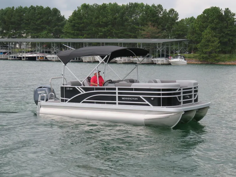 Slide: The Image of 2025 Bennington 20SVL-SPS pontoon boat cruising on a lake with lush green trees. - 8