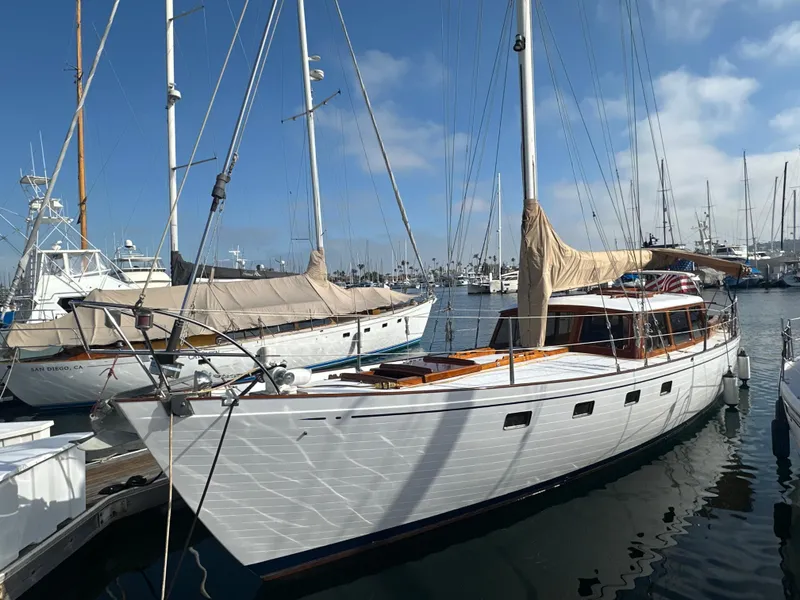 The Image of Sailing yacht Calkins 50 Pilot House, 1969, cruising near rocky coastline under clear blue sky. - 0